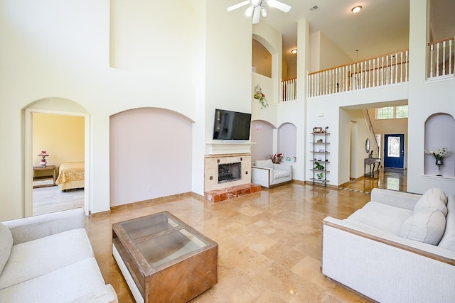 living area featuring a tile fireplace, a high ceiling, visible vents, baseboards, and ceiling fan