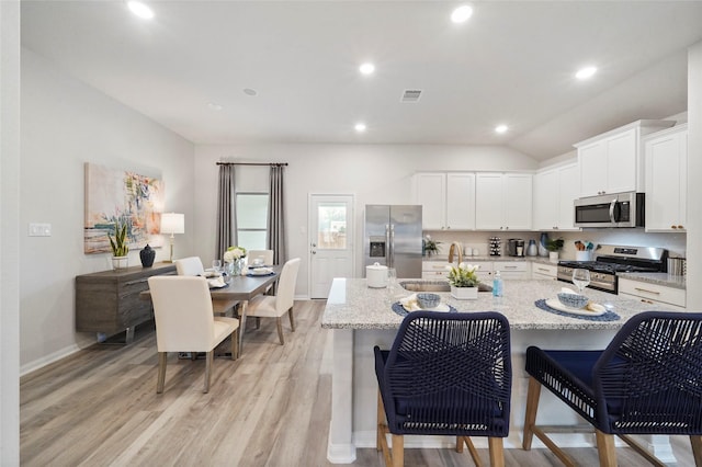 kitchen featuring a sink, stainless steel appliances, light wood-type flooring, visible vents, and an island with sink