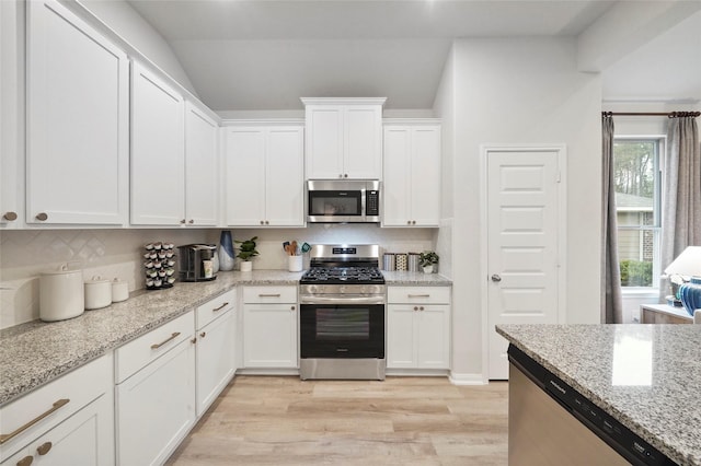 kitchen featuring light stone countertops, appliances with stainless steel finishes, tasteful backsplash, white cabinets, and light wood-type flooring