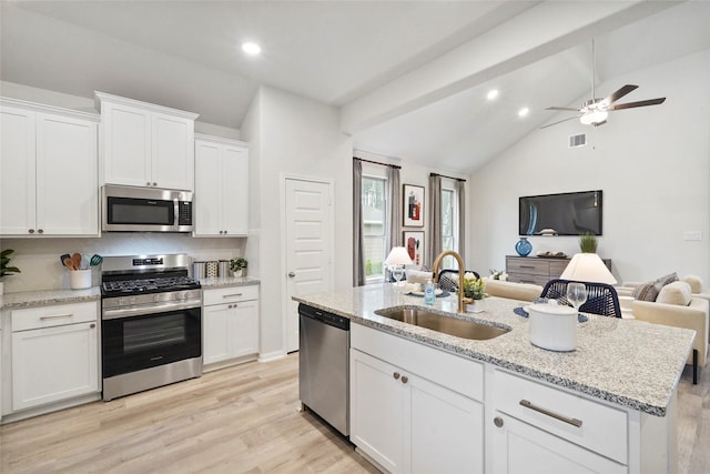 kitchen featuring a sink, open floor plan, white cabinets, appliances with stainless steel finishes, and lofted ceiling