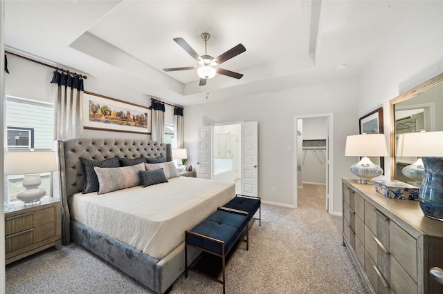 bedroom with a ceiling fan, connected bathroom, a raised ceiling, a spacious closet, and light colored carpet