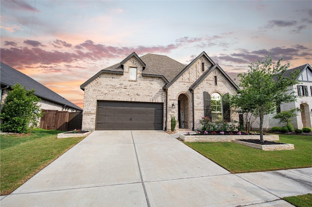 french country style house with a lawn, brick siding, fence, and concrete driveway