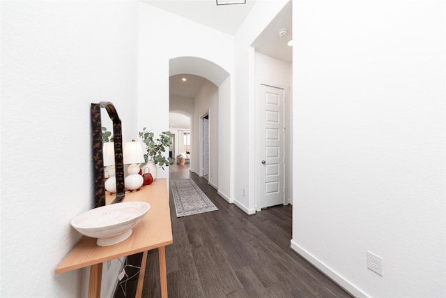 hallway featuring arched walkways, baseboards, dark wood finished floors, and recessed lighting