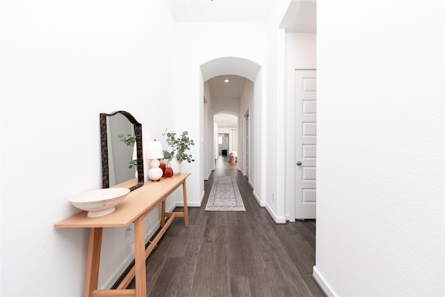 hallway featuring arched walkways, baseboards, and dark wood finished floors