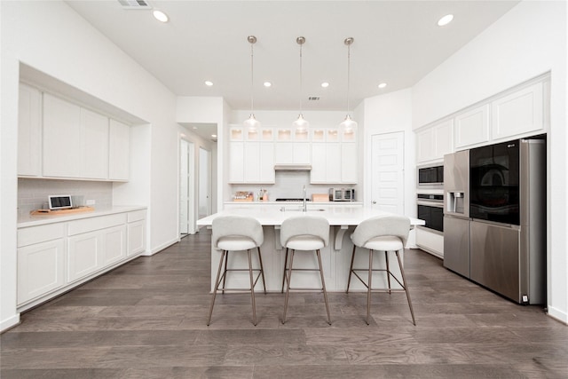 kitchen featuring glass insert cabinets, a kitchen bar, stainless steel appliances, white cabinetry, and tasteful backsplash