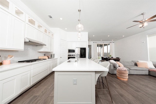 kitchen with under cabinet range hood, dark wood-style flooring, visible vents, open floor plan, and appliances with stainless steel finishes