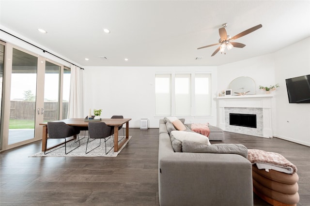 living area featuring a premium fireplace, a wealth of natural light, a ceiling fan, and dark wood-type flooring