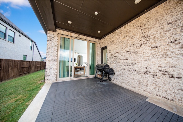 wooden terrace featuring a grill, fence, and a lawn