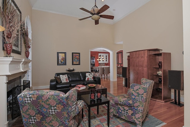 living room with wood finished floors, a ceiling fan, crown molding, baseboards, and arched walkways