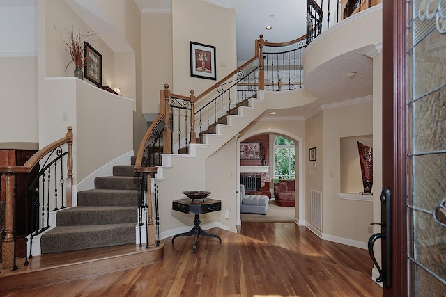 entrance foyer featuring crown molding, stairway, wood finished floors, and arched walkways