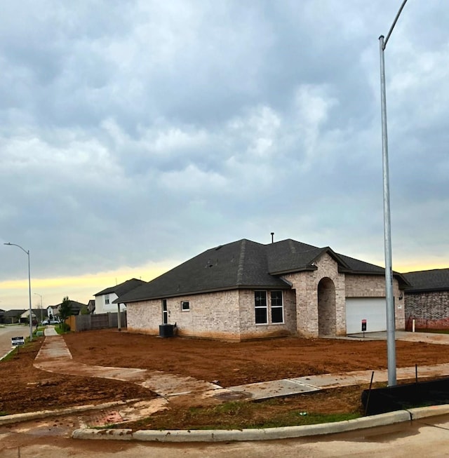 view of side of property with central air condition unit, roof with shingles, an attached garage, and brick siding