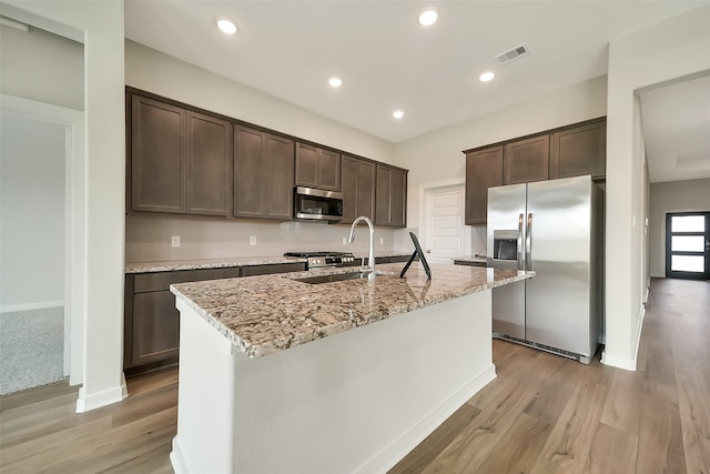 2563 Newport Breeze Dr, Katy, TX 77493 - kitchen with stainless steel appliances, dark brown cabinets, a sink, light stone countertops, and light wood finished floors