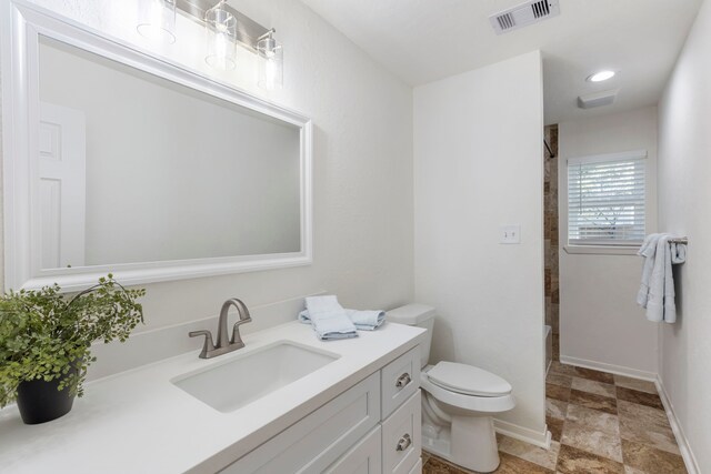 full bathroom featuring toilet, tiled shower, vanity, and visible vents