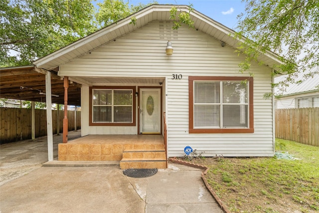 bungalow-style house with an attached carport, a porch, driveway, and a fenced backyard