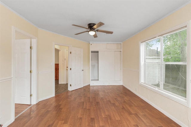 empty room with a ceiling fan, baseboards, crown molding, and wood finished floors