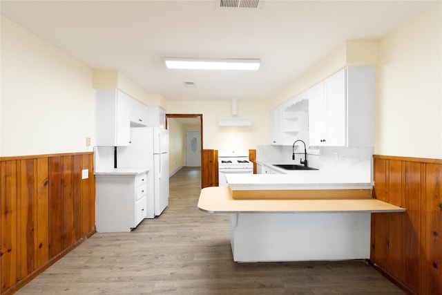 kitchen with a sink, a peninsula, white appliances, and light countertops