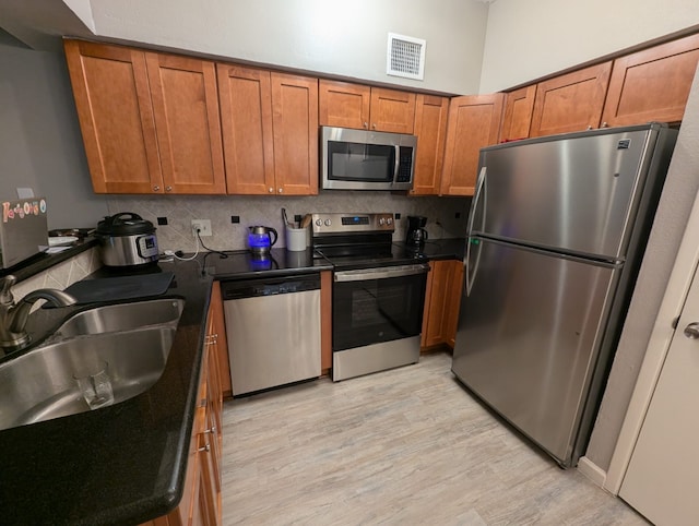 2626 Holly Hall St Unit 1201, Houston, TX 77054 - kitchen with stainless steel appliances, a sink, brown cabinetry, dark countertops, and light wood-type flooring