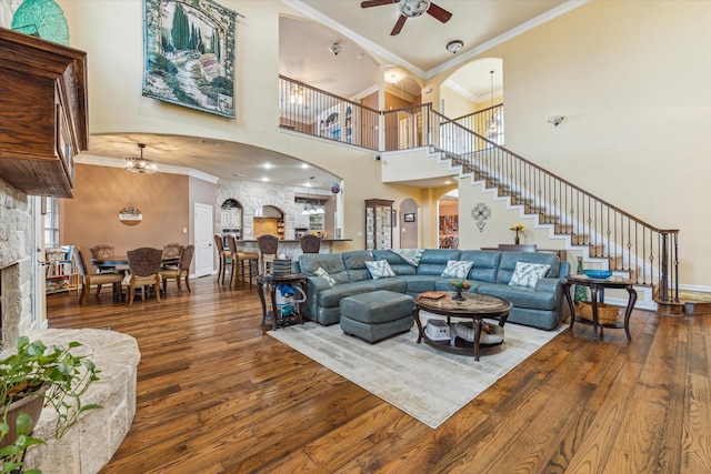 living area with wood finished floors, a high ceiling, crown molding, ceiling fan, and arched walkways