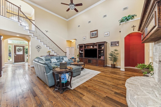 living area featuring hardwood / wood-style floors, stairway, a ceiling fan, arched walkways, and a high ceiling