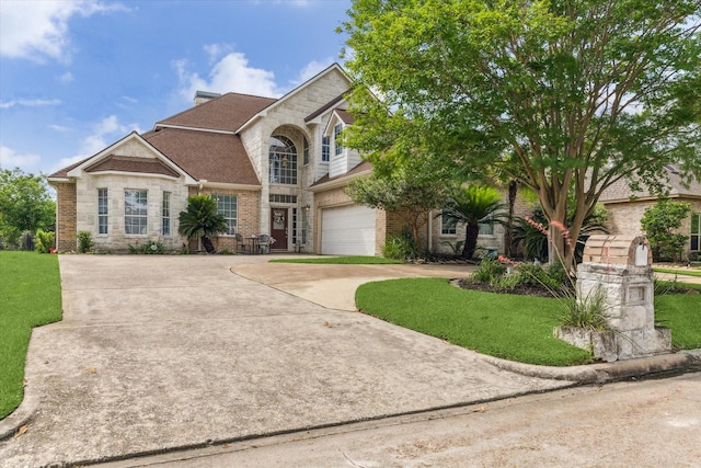 view of front of property featuring driveway, stone siding, an attached garage, a front lawn, and brick siding