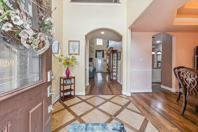 foyer entrance with arched walkways, inlaid floor details, light wood finished floors, and baseboards