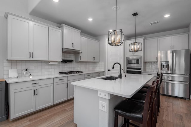 17828 Hanson Ridge Dr, Conroe, TX 77316 - kitchen with stainless steel appliances, a sink, a chandelier, light wood-style flooring, and decorative backsplash