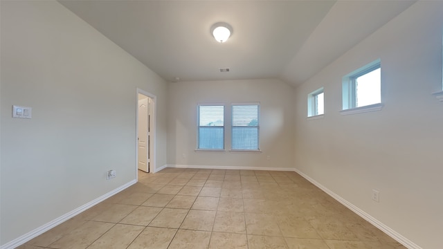 empty room with lofted ceiling, light tile patterned flooring, baseboards, and visible vents
