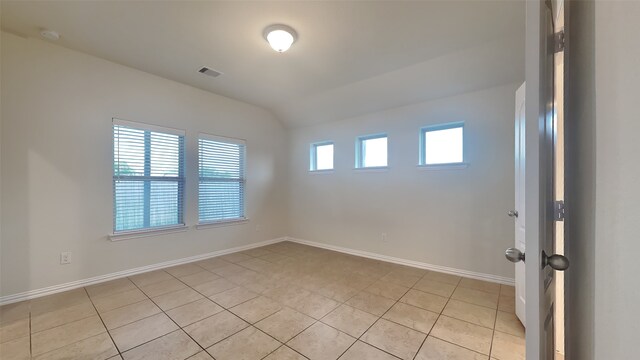 empty room featuring vaulted ceiling, baseboards, light tile patterned floors, and visible vents