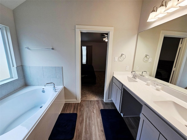 ensuite bathroom with double vanity, connected bathroom, wood finished floors, and a sink