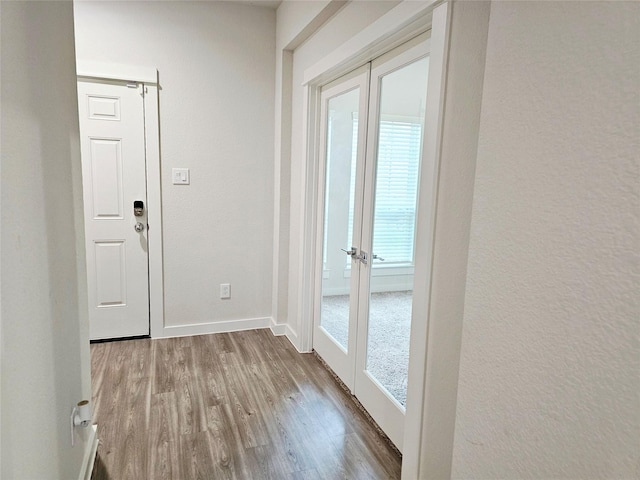 doorway featuring wood finished floors, baseboards, and a textured wall