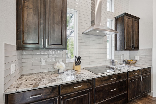 3419 Campestres, Spring Branch, TX 78070 - kitchen featuring black electric stovetop, light stone counters, wall chimney exhaust hood, dark brown cabinetry, and decorative backsplash