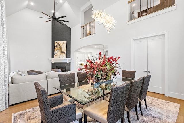 203 S Empress Green Pl, Montgomery, TX 77316 - dining room with wood finished floors, ceiling fan with notable chandelier, high vaulted ceiling, arched walkways, and a warm lit fireplace