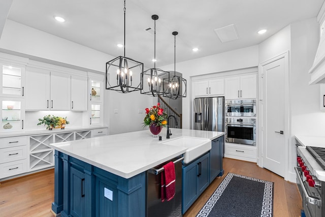 203 S Empress Green Pl, Montgomery, TX 77316 - kitchen with stainless steel appliances, blue cabinets, a sink, light countertops, and white cabinets