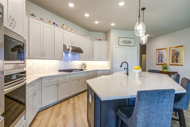 9823 Starry Night Ln, Manvel, TX 77578 - kitchen with light wood-type flooring, a breakfast bar area, under cabinet range hood, light countertops, and appliances with stainless steel finishes