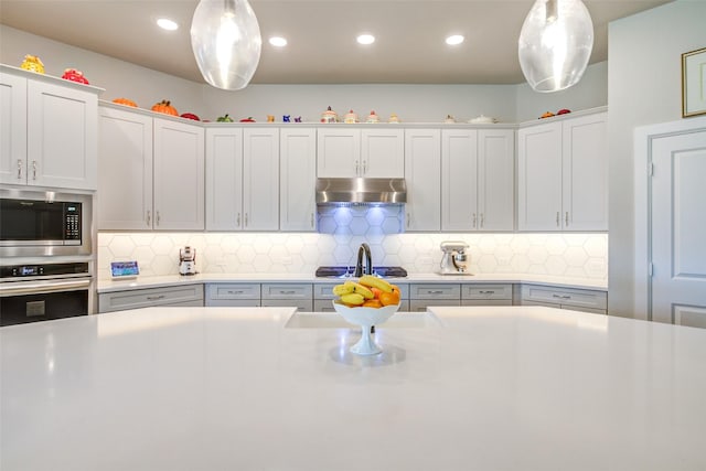 9823 Starry Night Ln, Manvel, TX 77578 - kitchen featuring stainless steel appliances, under cabinet range hood, decorative light fixtures, decorative backsplash, and light countertops