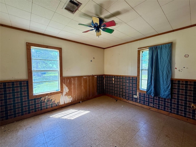 unfurnished room with ornamental molding, visible vents, ceiling fan, and a wainscoted wall
