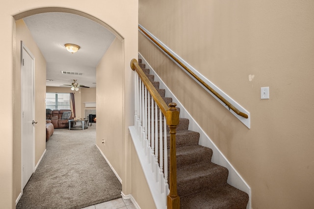 7210 Avocet Ln, Houston, TX 77040 - stairway with carpet flooring, visible vents, ceiling fan, arched walkways, and a warm lit fireplace