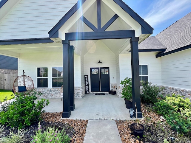 entrance to property featuring stone siding, covered porch, and fence
