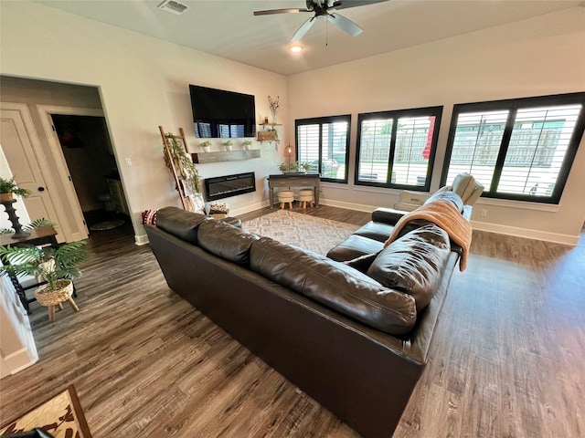 living room featuring wood finished floors, visible vents, a ceiling fan, baseboards, and a glass covered fireplace