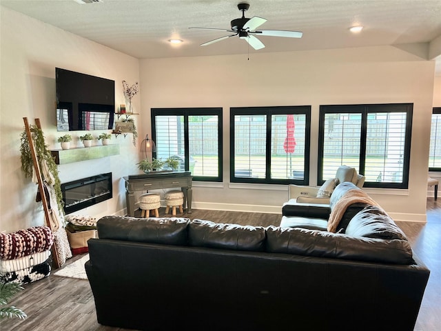 living area with baseboards, a ceiling fan, a glass covered fireplace, and wood finished floors