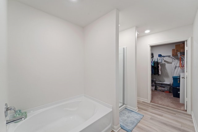 bathroom with baseboards, a bath, a shower stall, wood finished floors, and a spacious closet