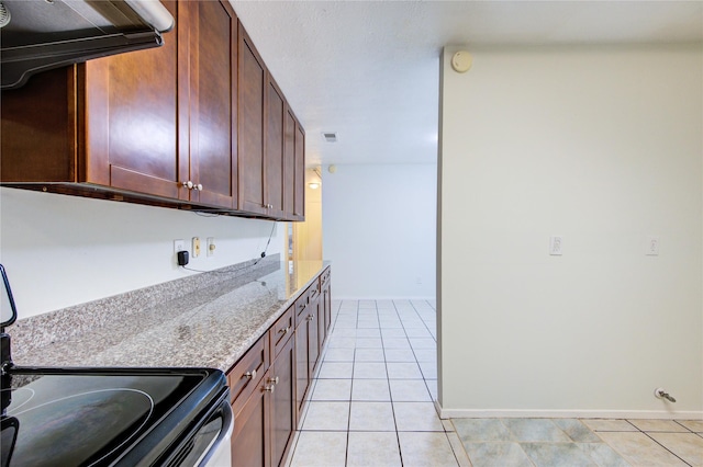 kitchen featuring light tile patterned floors, baseboards, light stone countertops, and range with electric cooktop