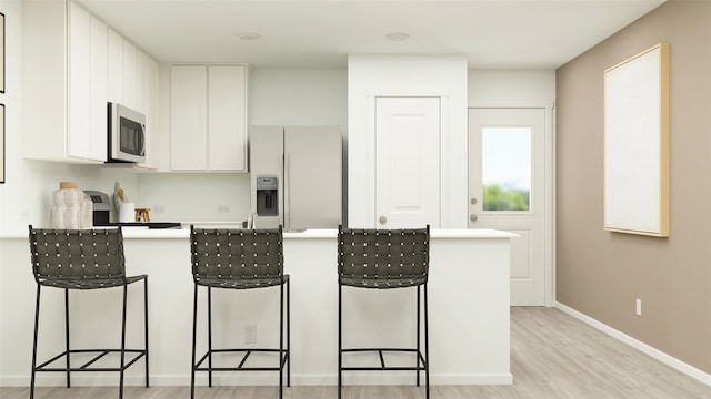 kitchen featuring a breakfast bar area, light countertops, light wood-style flooring, white fridge with ice dispenser, and stainless steel microwave