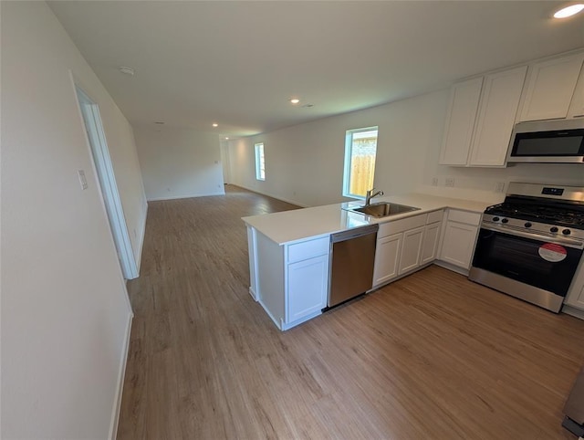 kitchen with light wood finished floors, a sink, white cabinetry, open floor plan, and appliances with stainless steel finishes