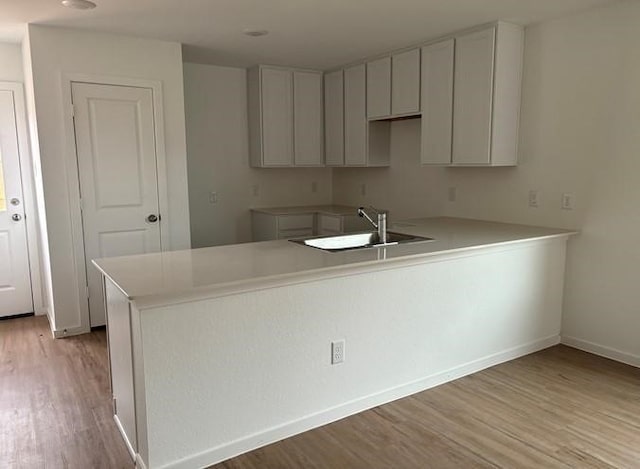 kitchen with a peninsula, a sink, baseboards, light countertops, and light wood-style floors