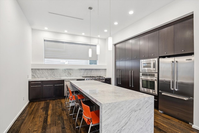 kitchen featuring a center island, a breakfast bar, dark wood-type flooring, backsplash, and appliances with stainless steel finishes