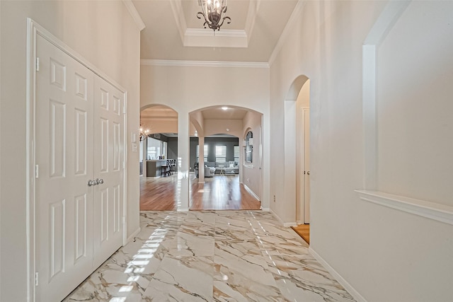corridor with a tray ceiling, baseboards, marble finish floor, crown molding, and arched walkways