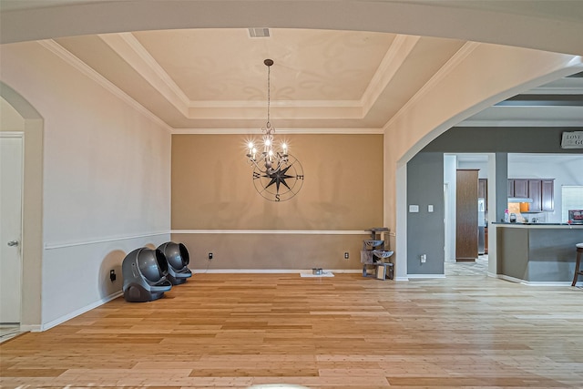 interior space featuring an inviting chandelier, light wood-style floors, a raised ceiling, and arched walkways