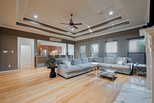 living room with a ceiling fan, a tray ceiling, ornamental molding, light wood finished floors, and visible vents