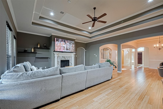 living room featuring ceiling fan with notable chandelier, a tray ceiling, a fireplace, visible vents, and arched walkways